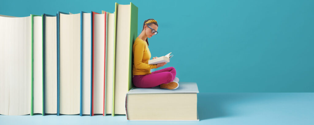 Woman reading a book, next to a stack of other books.